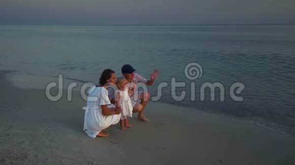 家人在海滩上散步父母和他们的小女儿沿着海滨散步父母蹲在他们身边视频的预览图