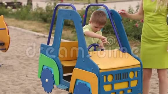 一个小男孩坐着玩具车在操场上玩他妈妈站在旁边视频的预览图