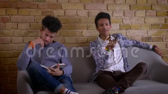 两个年轻的男性朋友坐在舒适的公寓里的沙发上的特写镜头非裔美国人视频的预览图