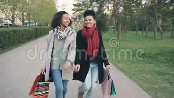 多利拍摄了两个迷人的混合种族妇女跳舞并玩得开心而步行下公园与购物袋快乐视频的预览图