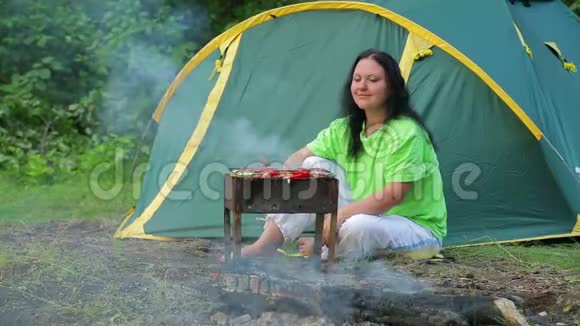 一个年轻的女人坐在一个帐篷背景的森林里在她的胸罩上准备晚餐总体计划视频的预览图
