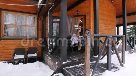 年轻的一家人在漂亮房子的阳台上喝热饮料视频的预览图