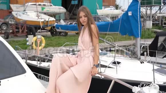 一个穿着裙子的迷人女孩坐在栏杆上的船上用慢镜头拍摄视频的预览图