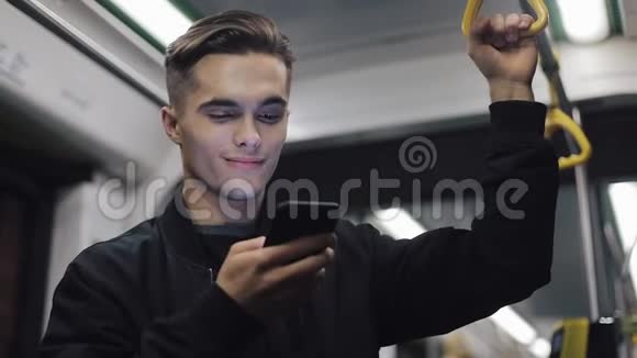 英俊男子的肖像持有扶手浏览智能手机在公共交通他读了好消息视频的预览图