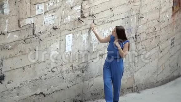 一个年轻的女孩在度假小镇上检查一堵旧墙视频的预览图