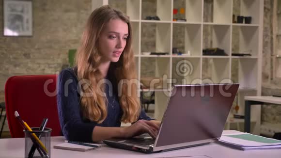 一幅金发美女漂亮的白种人女商人在办公室里用笔记本电脑在视频聊天的肖像视频的预览图