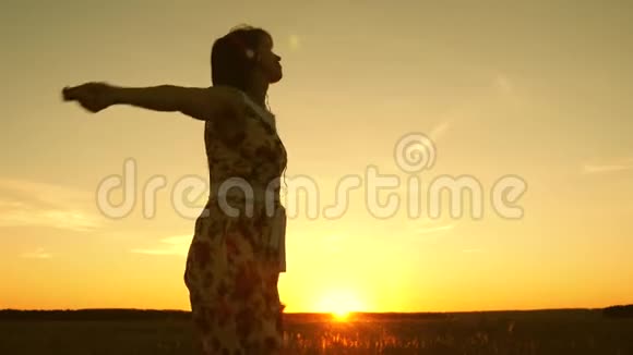 快乐的女孩听着音乐在美丽的日落的光线中跳舞天空戴着耳机的年轻女孩视频的预览图