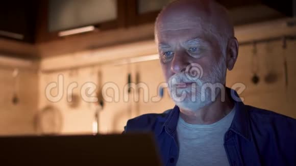 老人晚上从家里办公室用笔记本电脑工作自由职业者晚上用手机聊天视频的预览图