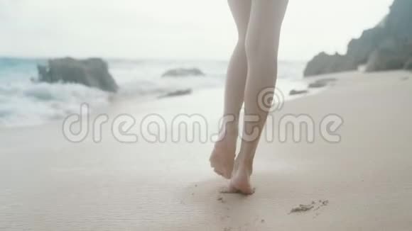 慢动作靠近雌腿沿着海浪背景的沙滩行走稳定射击视频的预览图