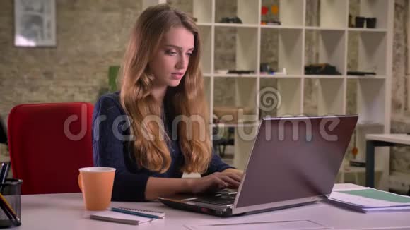 一幅美丽的金发白种人女商人在办公室里用笔记本电脑和喝咖啡的肖像视频的预览图