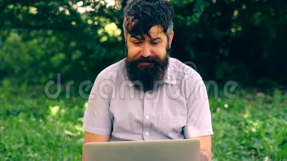 有趣的胡子男在公园里用笔记本电脑工作自由或远程工作在线聊天的概念视频的预览图