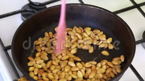 一个人把去皮杏仁和一把铲子混合在热煎锅上去干杏仁用来填充巧克力釉面糖果视频的预览图