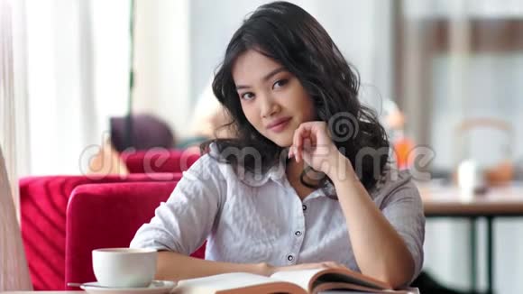 亚洲年轻的女学生享受着与书和咖啡坐在一起的自由时光视频的预览图