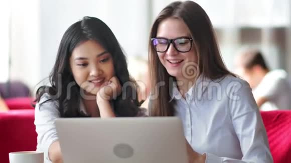两个年轻的微笑女商人朋友用笔记本电脑举行非正式团队会议视频的预览图