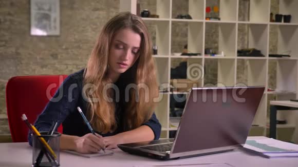 白种人金发女商人的肖像她专心地用笔记本电脑工作并在办公室做笔记视频的预览图