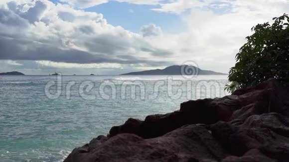 塞舌尔普拉斯林岛泡沫波浪在沙滩上翻滚前景中的石头慢动作视频的预览图