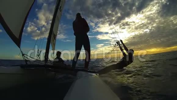 三个人在帆板双体船和日落天空上航行的剪影视频的预览图