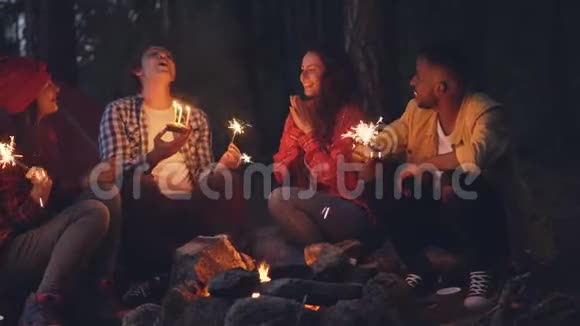 年轻女子在森林里庆祝生日朋友在蛋糕上吹蜡烛在人们面前拍手视频的预览图