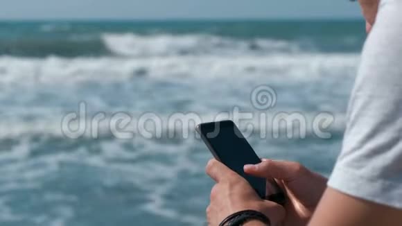 年轻人在坐在海边的大石头上的手机上输入一条信息视频的预览图
