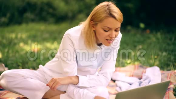 带着笔记本电脑在草坪上的女孩本科生在草地上坐着正在通过上网本做作业视频的预览图