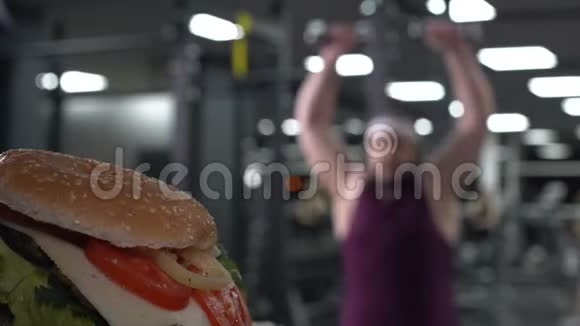 胖乎乎的男人用哑铃跳着看着美味的汉堡个人动机视频的预览图