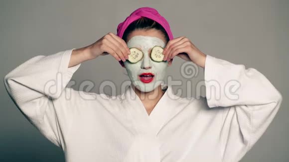 一个女孩脸上戴着面具头上戴着毛巾用黄瓜闭上眼睛笑美丽的女孩视频的预览图