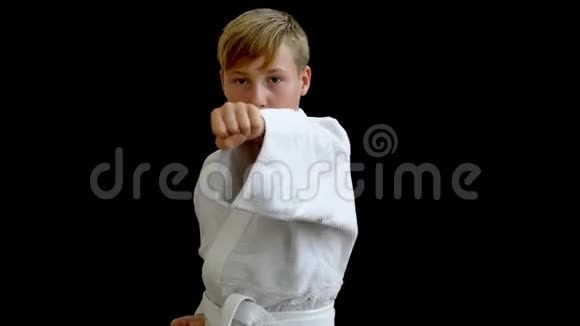 一个穿着白色和服的男孩展示了一个运动踢在黑暗背景下的运动员向前投掷一只手臂第二只手臂视频的预览图
