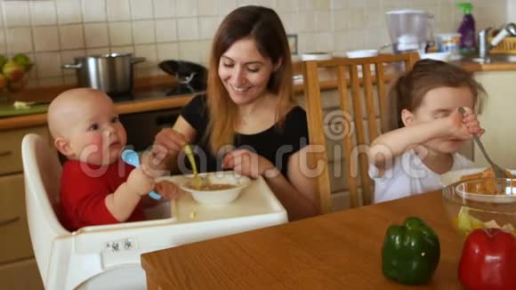 聪明的家庭主妇在厨房里喂她的两个孩子那孩子坐在椅子上一屁股坐进盘子里视频的预览图