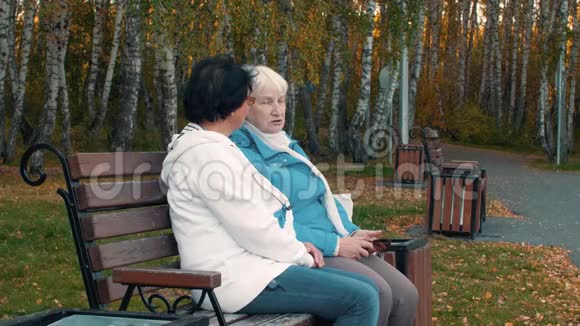 秋市的一位老妇人坐在长凳上和朋友聊天视频的预览图