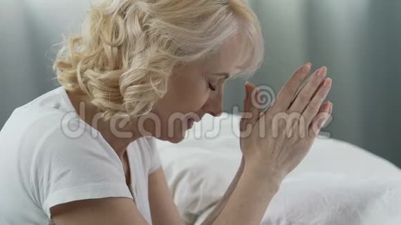 老年妇女在床上祈祷闭上眼睛微笑感谢上帝视频的预览图