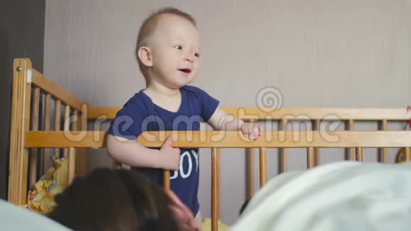 婴儿站在家里的婴儿床上小男孩学着站在婴儿床上妈妈睡觉视频的预览图