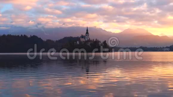 以阿尔卑斯山山脉为背景的斯洛文尼亚小岛布莱德湖和教堂的空中日落景色视频的预览图