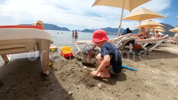 可爱的微笑的2岁男孩在海边玩沙子的4K镜头视频的预览图