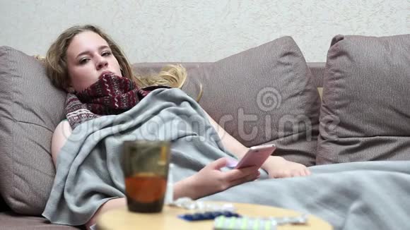 少女饮药茶暖躺在沙发上用智能手机视频的预览图