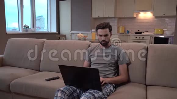 男人坐在沙发上拿着笔记本电脑他在家工作他很集中他不分散注意力男人看着屏幕视频的预览图