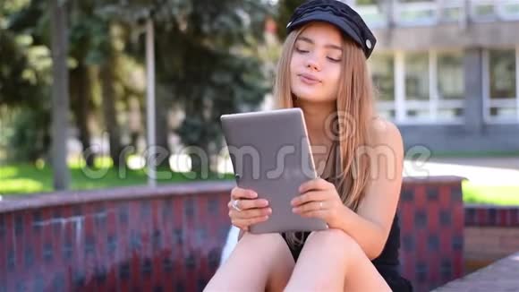 年轻的金发女郎坐在平板电脑的长凳上工作校园公园使用无线互联网的女大学生视频的预览图