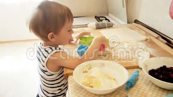 三岁男孩将樱桃放入面团并撒上面粉的4K镜头小厨师的概念视频的预览图
