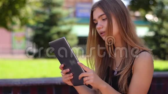 年轻的金发女郎坐在平板电脑的长凳上工作校园公园使用无线互联网的女大学生视频的预览图