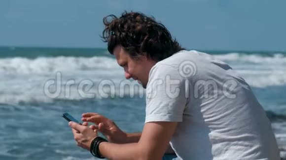 年轻人在坐在海边的手机上输入一条信息视频的预览图