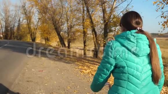 女孩在路上骑自行车旅行运动少年骑自行车一个穿绿色夹克的年轻女孩骑自行车上路视频的预览图