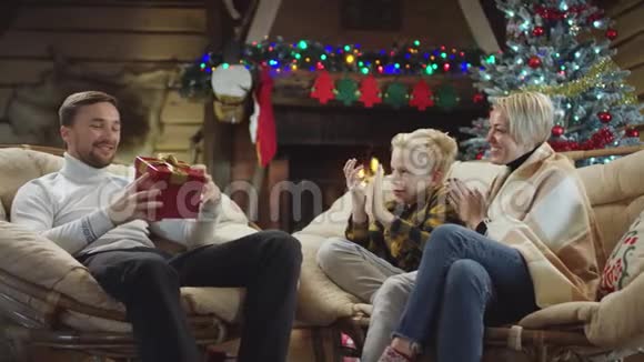 大胡子男人看着他的圣诞礼物坐着妻子和儿子他们拍手视频的预览图