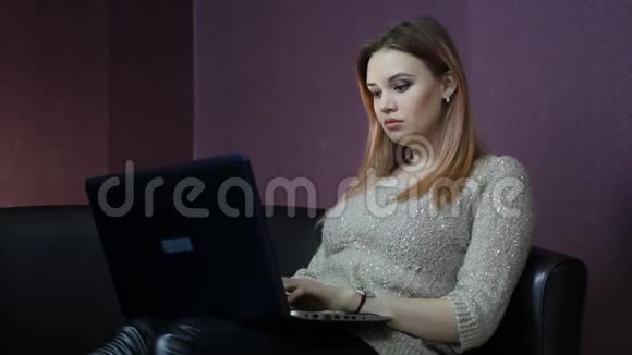 一个年轻的女人坐在一张小沙发上在电脑前工作视频的预览图