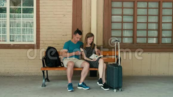 一对夫妇正在等待带电话和书的火车技术与传统视频的预览图