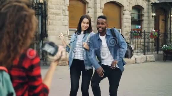 有创意的女孩和男人的朋友正在摆姿势拍照站在街上而带背包的年轻女人正在拍照视频的预览图
