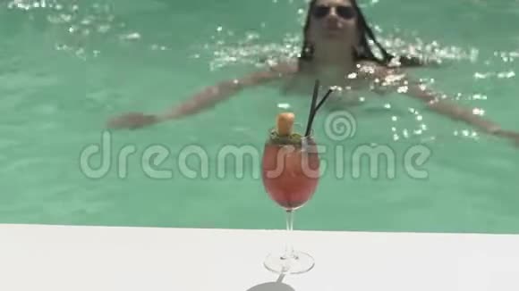 粉红色的鸡尾酒站在泳池边女人游到玻璃杯里去喝美丽女士的休闲视频的预览图