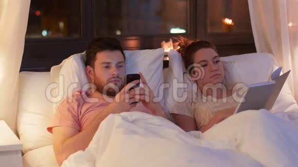 带智能手机的情侣晚上在床上看书视频的预览图