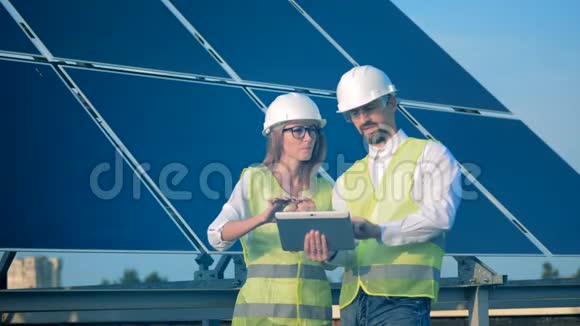 两名工程师在建筑屋顶的太阳能电池板附近工作可再生能源概念视频的预览图