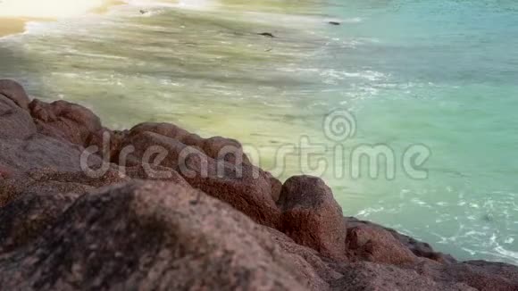 塞舌尔普拉斯林岛泡沫波浪在沙滩上翻滚前景中的石头慢动作视频的预览图