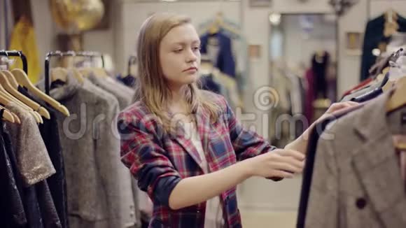 年轻漂亮的女人试穿一件连衣裙在服装店里看着相机视频的预览图