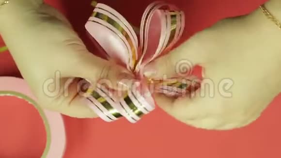 女人双手伸直粉红色丝带礼物蝴蝶结的花瓣给它蝴蝶结的形状红色背景视频的预览图